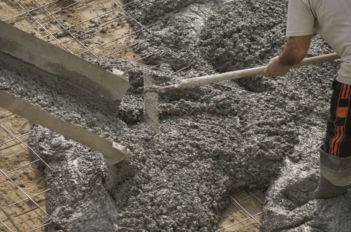 Concrete contractor spreading fresh concrete over steel reinforcement mesh